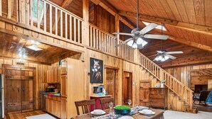 A wooden cabin interior with a dining area, kitchen, and staircase. - Welcome to M'Hollow, Cozy Cabin, Private Hot Tub, WiFi, and Screened in Porch (Logan)