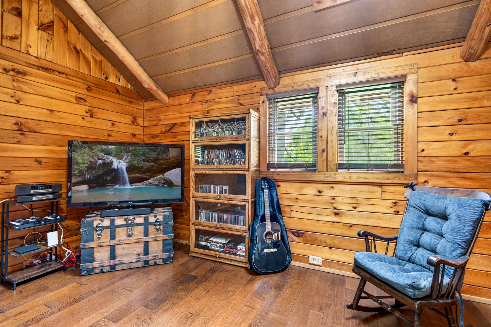 L’intérieur d’un chalet en bois, avec une télévision, une guitare, une bibliothèque et un fauteuil à bascule.