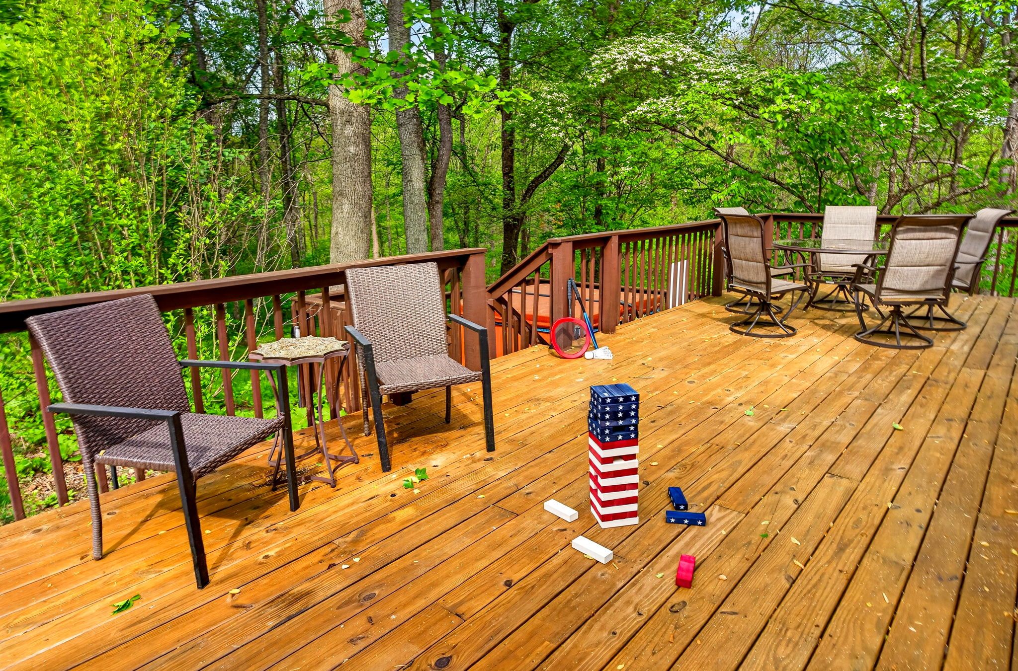A wooden deck with outdoor furniture, including chairs and a table, surrounded by trees.