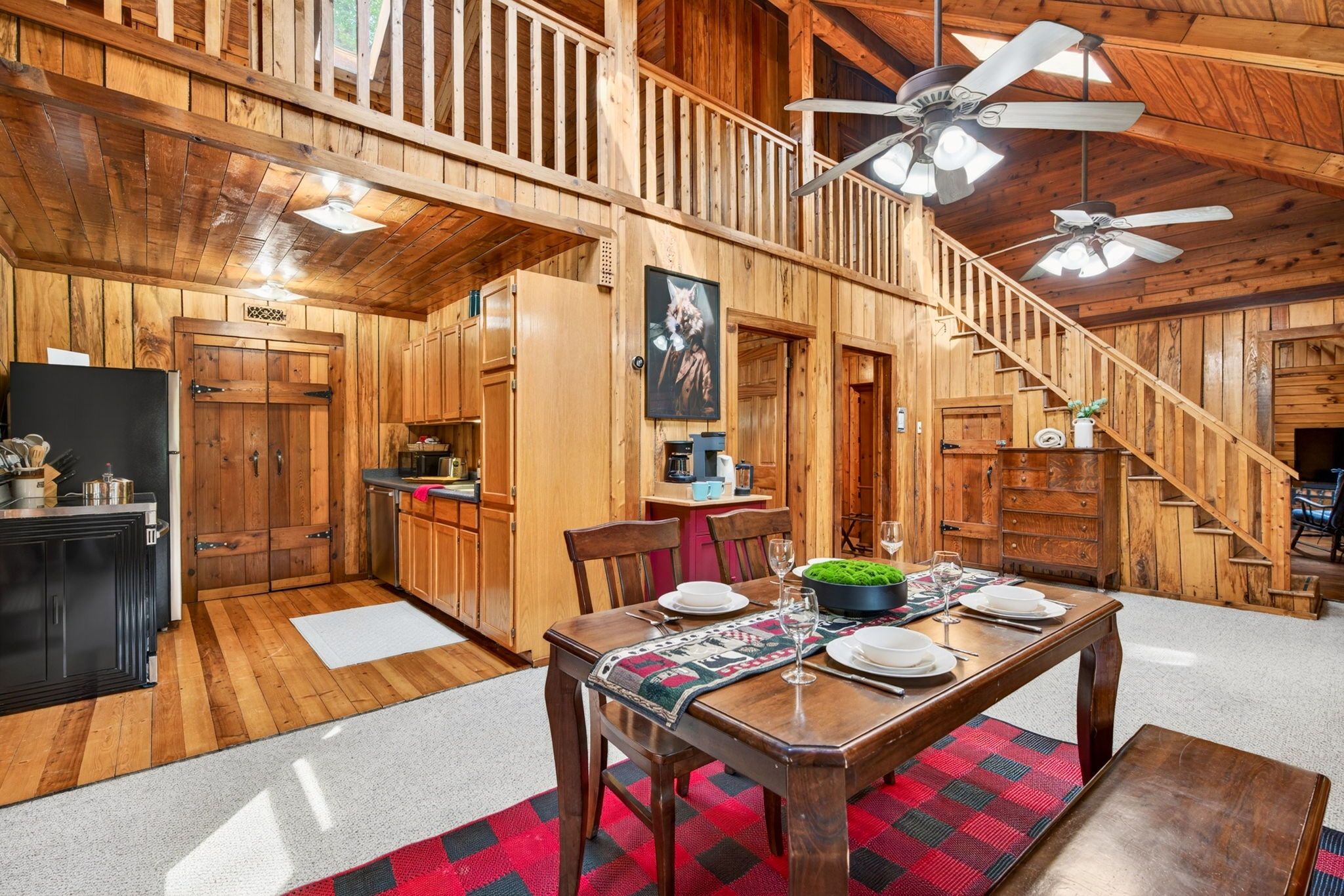 A wooden interior with a dining table set for four, a kitchen area, and a staircase.