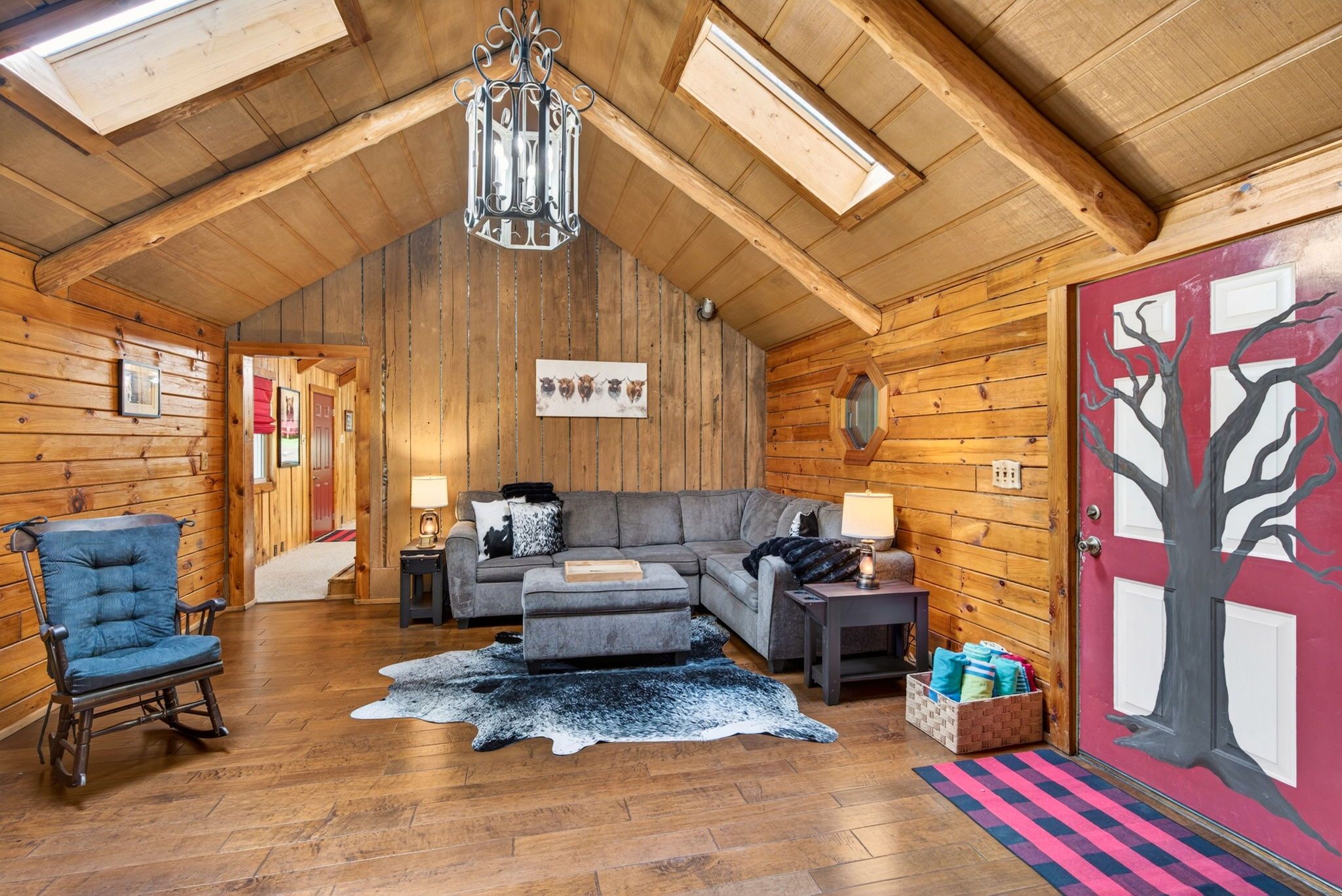 A cozy log cabin interior with a sofa, a rocking chair, a fireplace, and a door with a tree design.