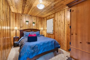 A wooden-paneled room with a bed, two bedside tables, a window, and a door.