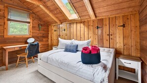 A wooden-paneled room with a bed, a desk, and a window.