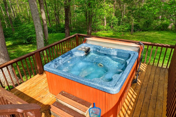 A hot tub on a wooden deck surrounded by trees.