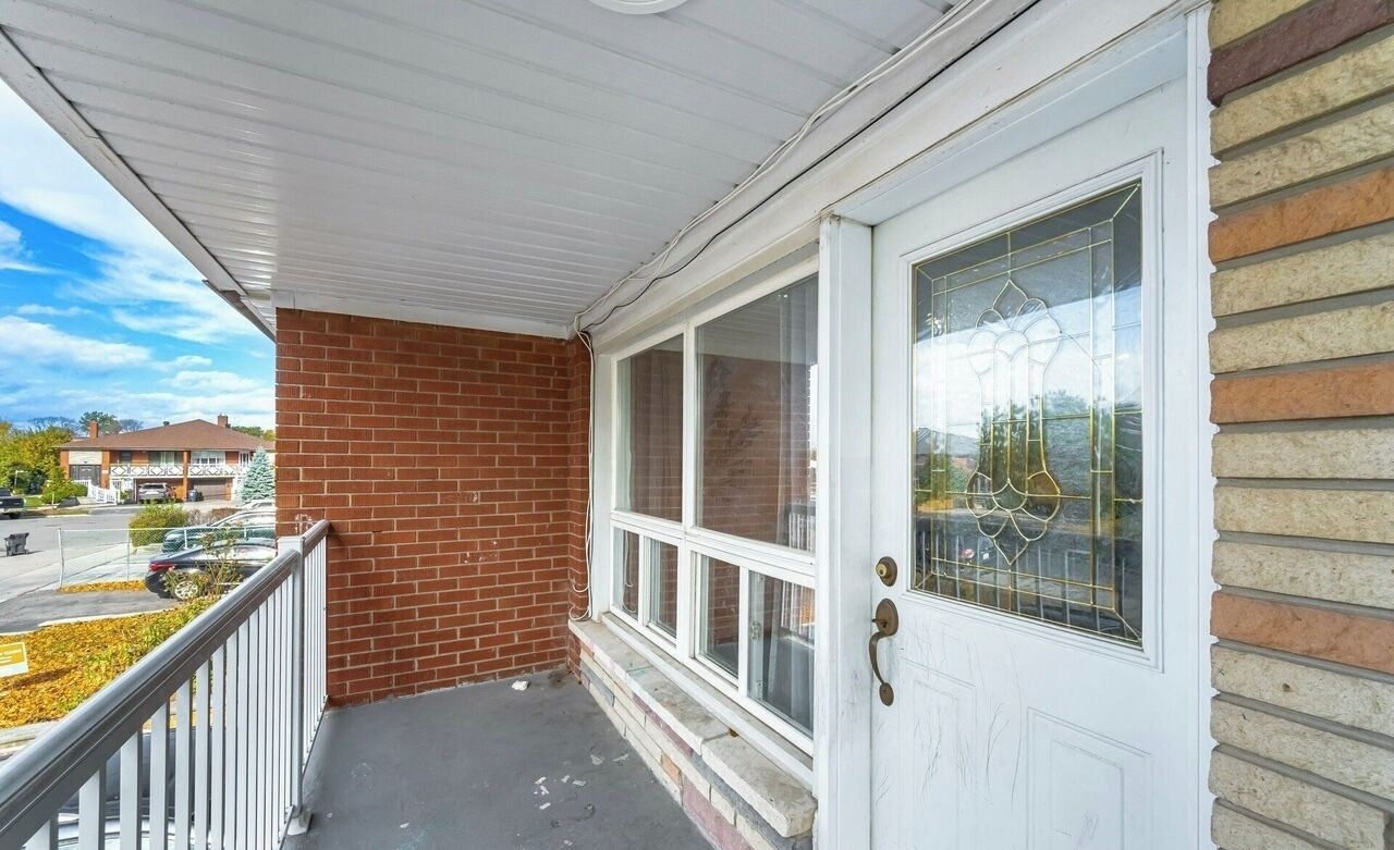 A residential porch with a white door, a brick wall, and a clear view of the street.