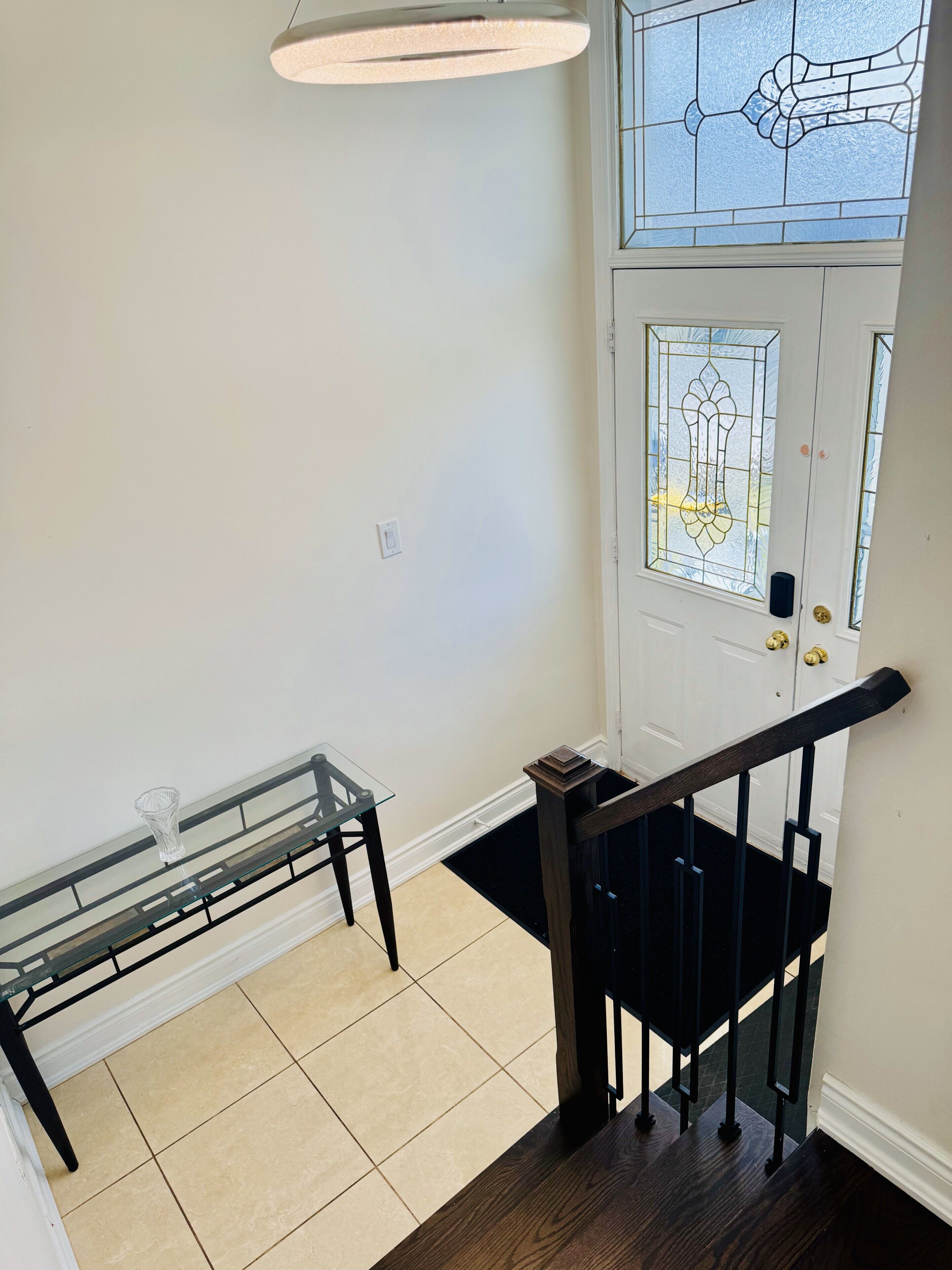 A staircase with a glass table and a door with stained glass.