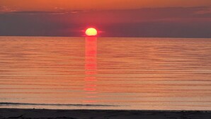 Solnedgang over et roligt hav med en strand i forgrunden.