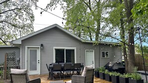 En terrasse med fletningsmøbler, grill og et hus med grå facade.