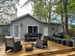 A deck with wicker furniture, a barbecue grill, and a house with a gray exterior. - Tulip Tree House in Shorewood-Tower Hills-Harbert, Michigan (Shorewood-Tower Hills-Harbert)