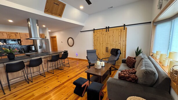 Et moderne køkken med en central ø, barstole, et spisebord med stole, en sofa og en loftsvifte.