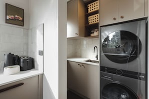 A modern kitchen with a built-in washer and dryer, a sink, and a tiled backsplash.
