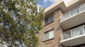 Un edifici de diverses plantes amb ranures per correu a la paret, un arbust i un cotxe estacionat a la façana.