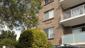 A multi-story building with mail slots on the wall, a hedge, and a car parked in front.