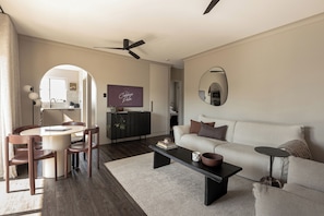 A modern living room with a dining area, a ceiling fan, a flat-screen TV, a sofa, and a coffee table.