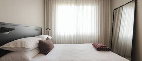 A neatly made bed with pillows, a bedside lamp, and a window with curtains.