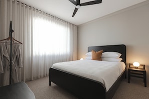 A hotel room with a bed, a bedside table with a lamp, a hanging coat rack, and a window with curtains. - The Cabbage Palm | Coastal Escape |
150m from Kiama's Main Street (Kiama)