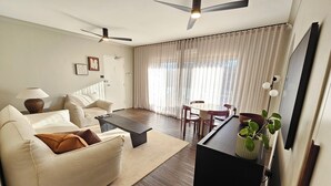 Un saló modern amb un sofà, una taula de centre, una taula de dinar, cadires, ventiladors de sostre i una televisió.
