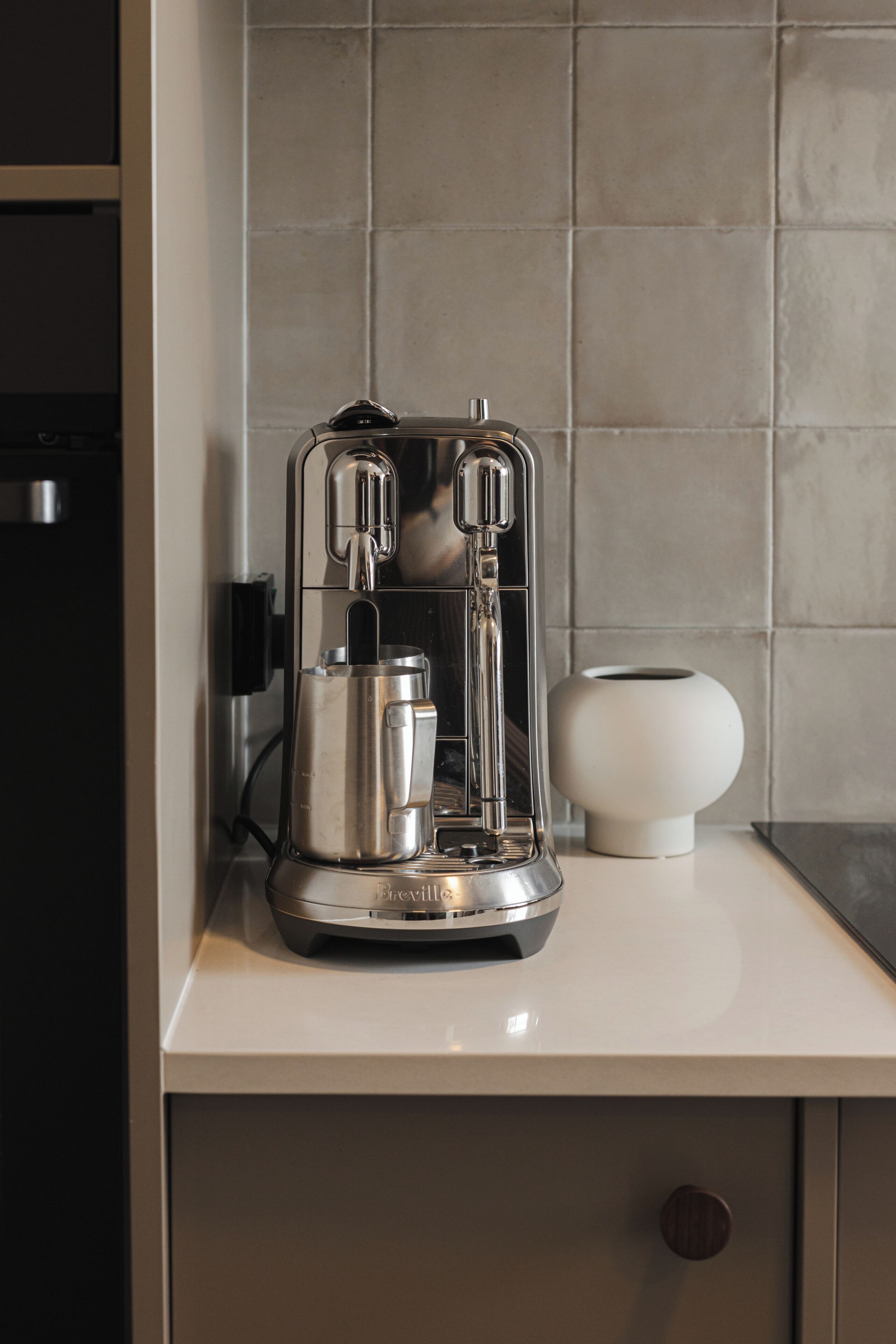 A kitchen with a coffee maker, a white vase, and a tiled backsplash.