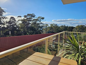A balcony with a red roof, glass railing, and a view of trees and buildings.