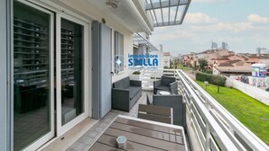 A balcony with outdoor furniture, a glass door leading to a room with shelves, and a city view. - Maricel residence °swimming pool#modern° (Lido di Jesolo)