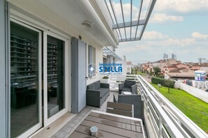A balcony with outdoor furniture, a glass door leading to a room with shelves, and a city view. - Maricel residence °swimming pool#modern° (Lido di Jesolo)