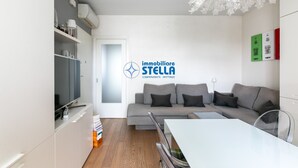 A modern living room with a grey sofa, a white dining table, and a ceiling light fixture. - Maricel residence °swimming pool#modern° (Lido di Jesolo)