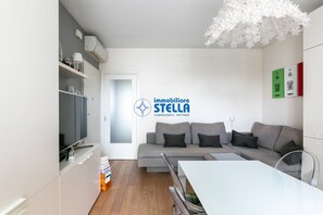 A modern living room with a grey sofa, a white dining table, and a ceiling light fixture. - Maricel residence °swimming pool#modern° (Lido di Jesolo)