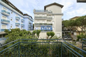 Un edificio a più piani con balconi, un cartello con la scritta 'immobiliare STELLA' e vegetazione circostante.