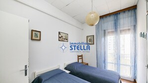 A bedroom with two beds, a wooden chair, a hanging light fixture, and a window with curtains. - Accogliente # trilocale 100mt from the sea# (Jesolo)