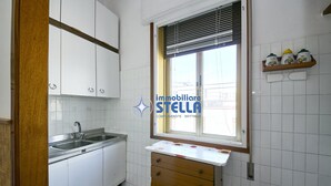 A kitchen with white cabinets, a double sink, a window with blinds, and a wooden countertop. - Accogliente # trilocale 100mt from the sea# (Jesolo)
