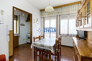 A dining area with a table, chairs, a television, and a kitchen in the background. - Accogliente # trilocale 100mt from the sea# (Jesolo)