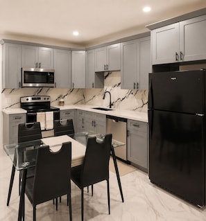 A modern kitchen with grey cabinets, a black refrigerator, a microwave, a stove, and a dining table with chairs. - FIFA World Cup ‘26! 2 Bedroom, 2.5 Bath (Houston)