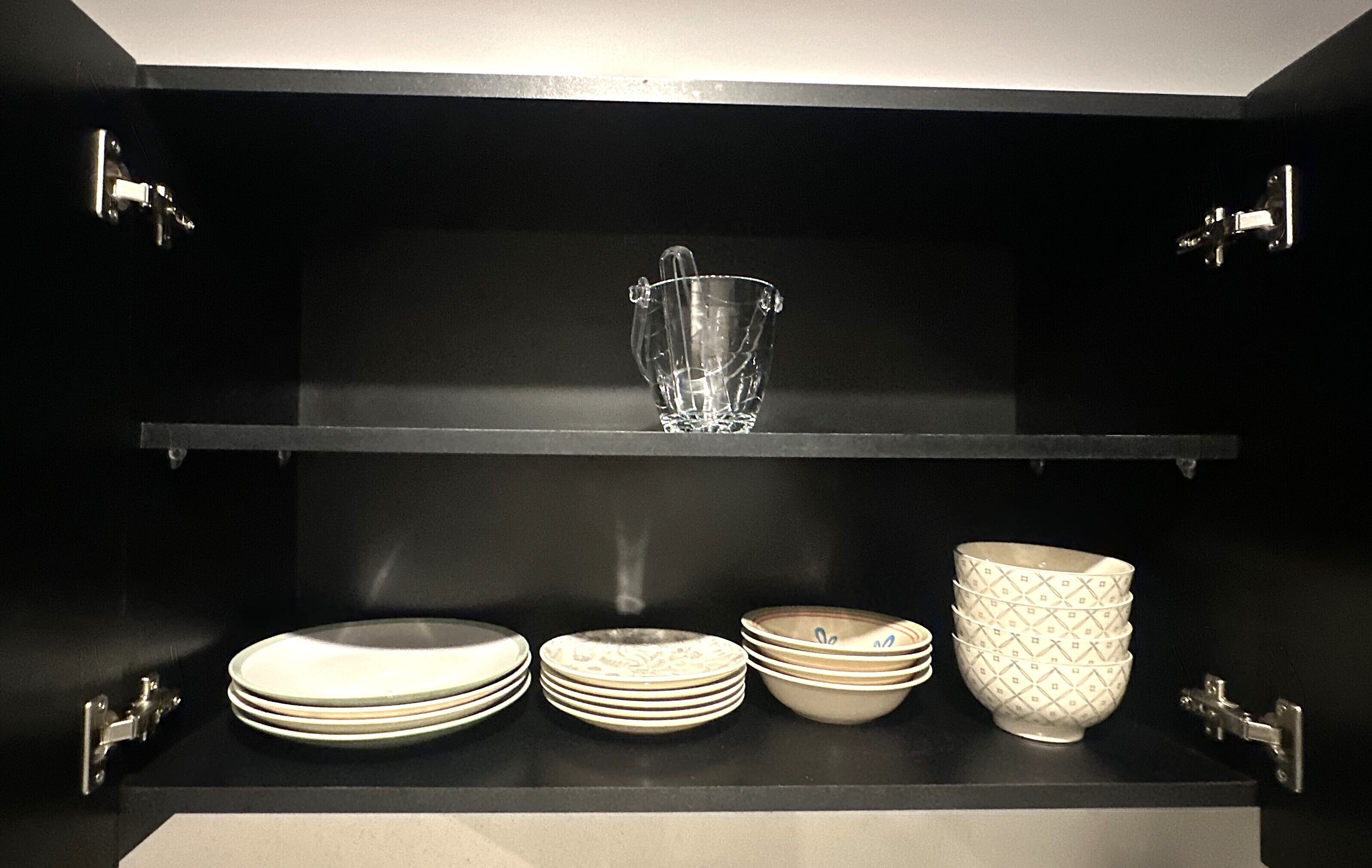 A black shelf with a clear glass vase, stacked plates, and patterned bowls.
