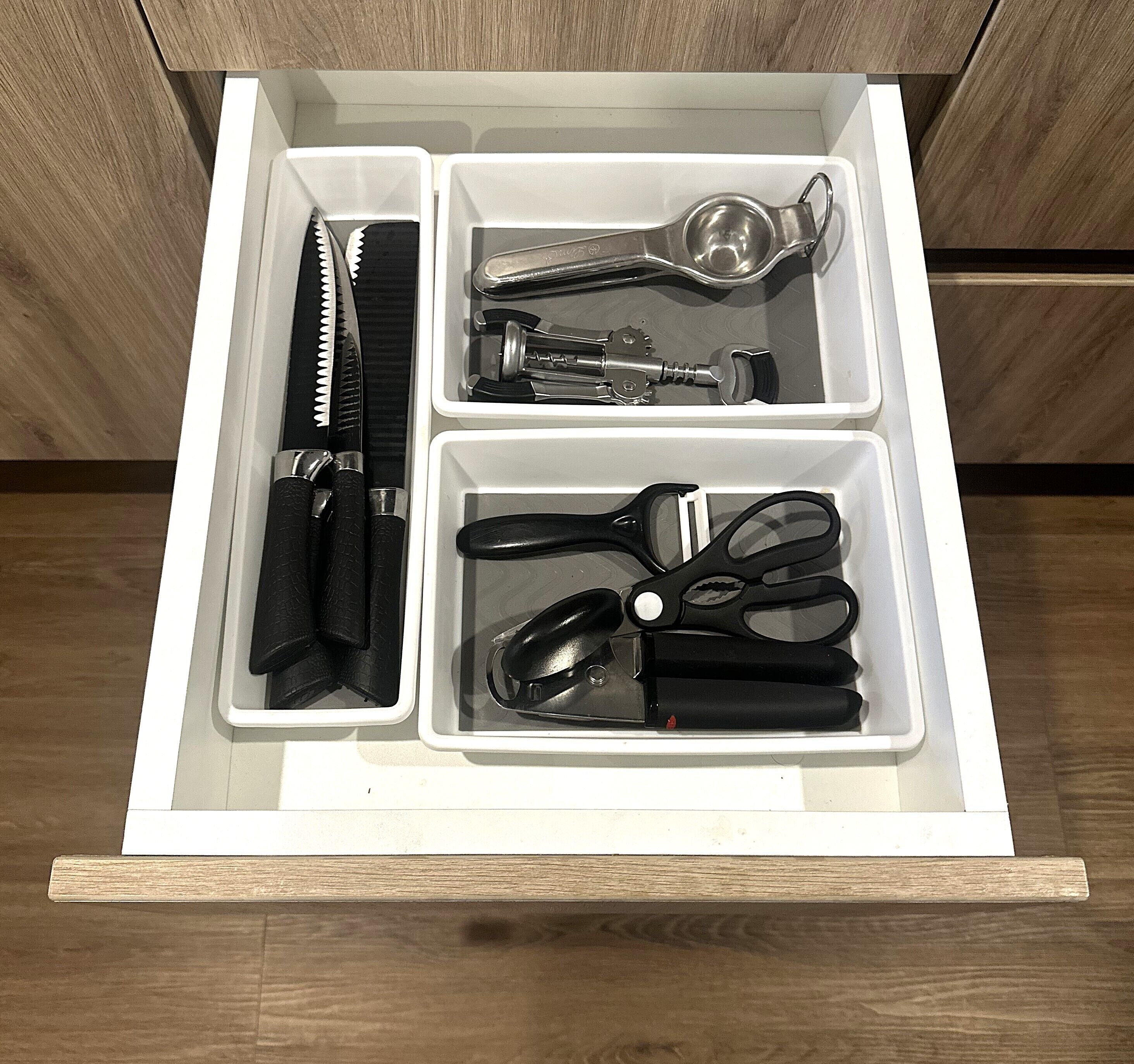 A drawer with compartments containing a knife, scissors, a bottle opener, and a can opener.