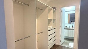 A walk-in closet with open shelving and drawers, a wooden floor, and a view into a bathroom with a sink and mirror. - Aparts4Days 2 Bedroom Apartment 4405 (Miraflores)