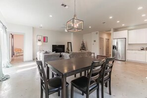 Une cuisine moderne avec des meubles blancs, un réfrigérateur en acier inoxydable et un coin repas comprenant une table et des chaises en bois foncé.