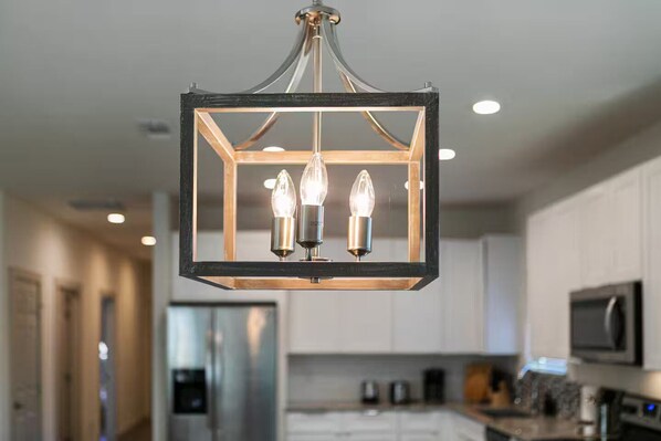 Une cuisine moderne dotée d’un luminaire suspendu, d’appareils électroménagers en acier inoxydable et de meubles blancs.