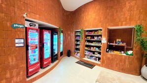 Un pasillo con paredes de ladrillo, máquinas expendedoras y estantes llenos de aperitivos, con un letrero que dice 'Plug'n Market'.