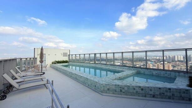 Una piscina en la azotea con vista a la ciudad, sillas de descanso y una pequeña construcción.