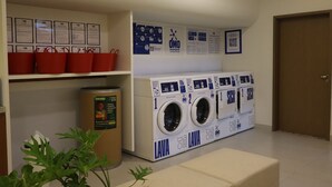 Zona de lavandería con lavadora y secadora de carga frontal, cestos rojos, carteles informativos y un contenedor de reciclaje.