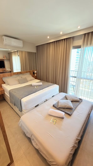 A hotel room with a large bed, a smaller bed, a TV, an air conditioner, and a balcony with a view. - Stay Refuge | Your retreat just minutes from the airport (Guarulhos)