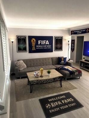 Ein Wohnzimmer mit Sofa, Couchtisch und Bannern zur FIFA Fussball-Weltmeisterschaft 2026.