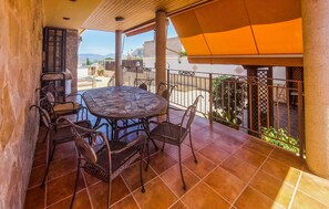 Un patio con un tavolo rotondo e sedie, vista sulla città e una zona coperta con ringhiera.