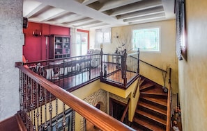 Un intérieur à plusieurs niveaux, avec un escalier, un mur rouge et une fenêtre à vitraux.
