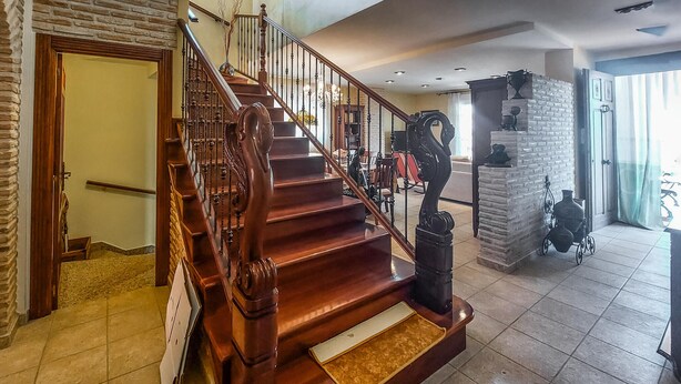 Una escalera de madera con barandilla, un pilar de piedra y un cochecito de bebé al frente.