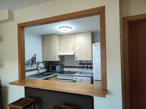 A kitchen with wooden cabinets, a microwave, an oven, and a sink. - Nice apartment with garage in Conil. (Conil De La Frontera)