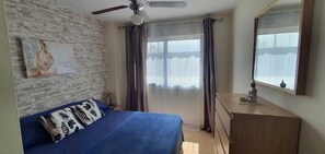 A bedroom with a bed, a ceiling fan, a dresser, a window with curtains, and a wall-mounted mirror. - Nice apartment with garage in Conil. (Conil De La Frontera)