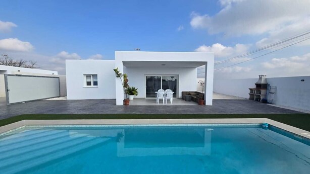 Ett modernt hus med en swimmingpool, en uteplats med stolar och ett område för grillning.