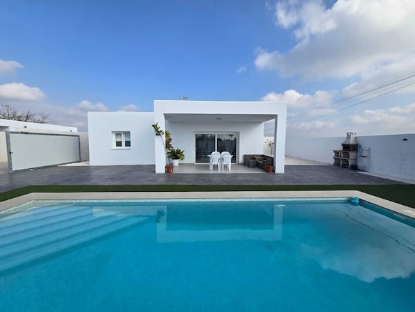 A modern house with a swimming pool, a patio with chairs, and a barbecue area. - Beautiful new house with private pool (Conil De La Frontera)
