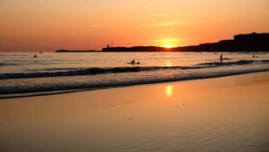En strand med vågor, en solnedgång och silhuetter av människor.
